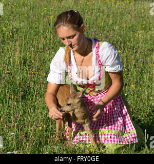 Woman in dirndl with a tame fawn in a flower meadow, Tyrol, Austria Stock Photo