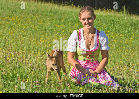 Woman in dirndl with a tame fawn in a flower meadow, Tyrol, Austria Stock Photo