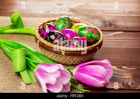 Beautiful background with painted Easter eggs in a wicker basket and lined with tulips on the background of burlap and old brown Stock Photo