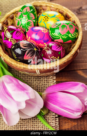 Beautiful background with painted Easter eggs in a wicker basket and lined with tulips on the background of burlap and old brown Stock Photo