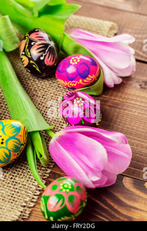 Beautiful background with painted Easter eggs and tulips laid on a background of burlap and old brown boards with free space for Stock Photo