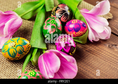 Beautiful background with painted Easter eggs and tulips laid on a background of burlap and old brown boards with free space for Stock Photo