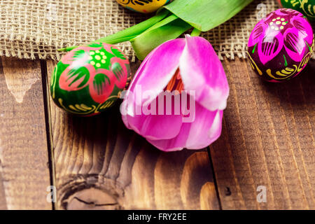 Beautiful background with painted Easter eggs and tulips laid on a background of burlap and old brown boards with free space for Stock Photo