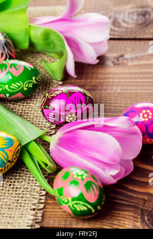 Beautiful background with painted Easter eggs and tulips laid on a background of burlap and old brown boards with free space for Stock Photo