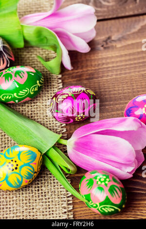 Beautiful background with painted Easter eggs and tulips laid on a background of burlap and old brown boards with free space for Stock Photo