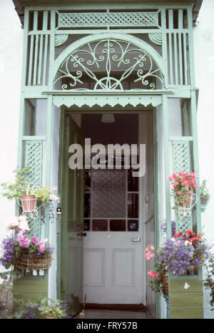 Hanging baskets on ornate porch on a half glazed stained glass Victorian front door Stock Photo