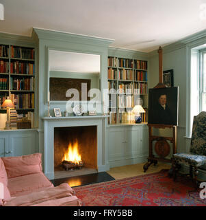 Mirror above fireplace with lighted fire in pale turquoise sitting room with an oil portrait on a wooden easel Stock Photo