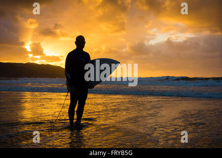 Las Palmas, Gran Canaria, Canary Islands, Spain, 24th March 2016. Weather: A surfer heading out for a late surf as the sun sets over Las Canteras beach in Las Palmas on Gran Canaria on a glorious Thurdsay in the Canary Islands; the day Prime Minister David Cameron and family arrived in the Canary Islands (Lanzarote) for their Easter holiday. Credit:  Alan Dawson News/Alamy Live News Stock Photo