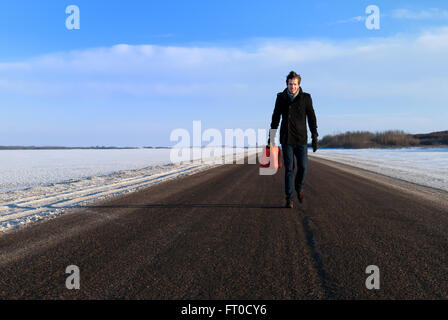 A Man Carries Gas Can on Empty Highway in Winter Stock Photo