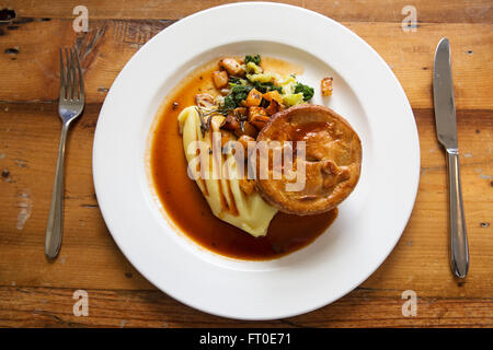 Venison pie served with mashed potatoe and seasonal vegetables in London, England. The meal is served with a pot of gravy. Stock Photo