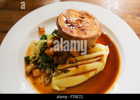 Venison pie served with mashed potatoe and seasonal vegetables in London, England. The meal is served with a pot of gravy. Stock Photo