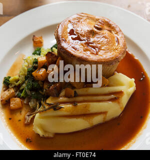 Venison pie served with mashed potatoe and seasonal vegetables in London, England. The meal is served with a pot of gravy. Stock Photo