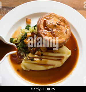 Venison pie served with mashed potatoe and seasonal vegetables in London, England. The meal is served with a pot of gravy. Stock Photo