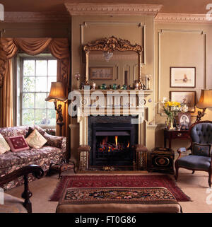 Ornate antique mirror above fireplace in Georgian style drawing room with lighted lamps Stock Photo