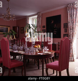 Pink upholstered chairs at table set for lunch in pink nineties dining room with tall vases of datura on the table Stock Photo