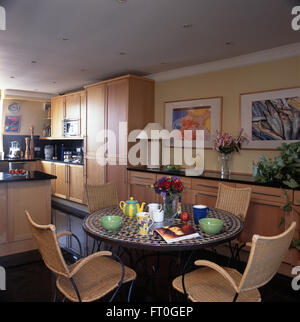 Wicker chairs and circular metal table with a mosaic tiled top in a nineties kitchen Stock Photo