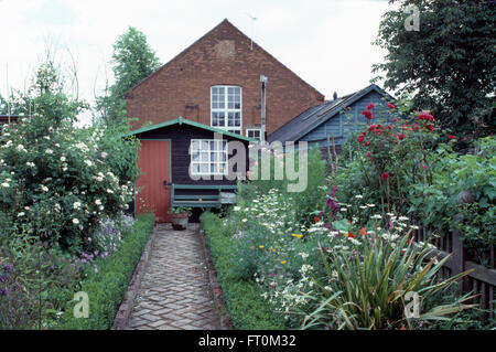 Herringbone brick paved path between borders with edged with box leading to wooden shed in garden of a country cottage Stock Photo