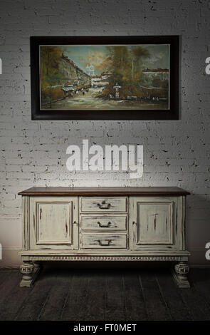 Still life of vintage white sideboard and hanged framed painting on a dark wooden floor and white bricks wall in studio Stock Photo