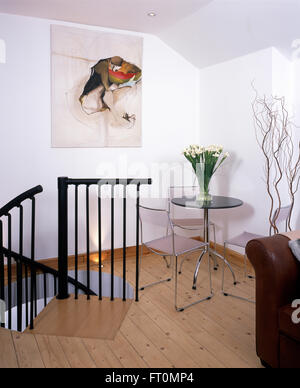 Stainless steel chairs and small tripod table in dining area of loft conversion apartment with wooden floor and metal banisters Stock Photo