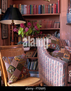 Tapestry patchwork cushions on a cane chair and Paisley patterned armchair beside bookshelves in pink living room Stock Photo
