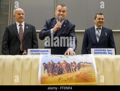 Expedition 47 Russian cosmonaut Alexei Ovchinin of Roscosmos, center, describes a poster created for him and his fellow crew members, NASA astronaut Jeff Williams, left, and Russian cosmonaut Oleg Skripochka during a crew press conference at the Gagarin Cosmonaut Training Center (GCTC), Friday, Feb. 26, 2016, in Star City, Russia.  The poster, a lighthearted take on the famous Russian painting &quot;Burlaki na Volge&quot; by Ilya Repin, depicts Ovchinin, Skripochka, and Williams as part of a crew of Burlaks, or barge haulers, dragging a barge on the Volga river. Ovchinin has chosen Burlak as t Stock Photo