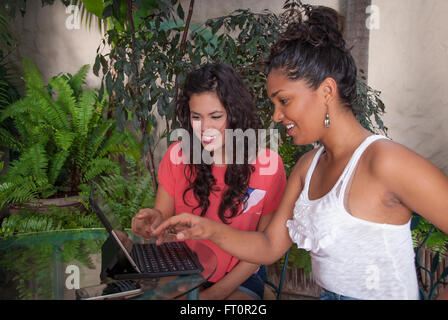 2 young Hispanic women use laptop on patio table  #613PV Stock Photo