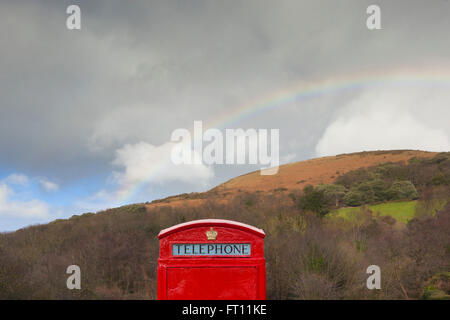 A traditional british red telephone box sits under a large rainbow arcing over Bossington hill in somerset. Stock Photo