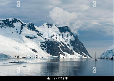 A sailing boat and snow-covered mountains, Lemaire Channel, near Graham Land Antarctica Stock Photo