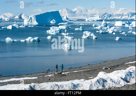 People walking along the rocky beach near Rothera Station with icebergs in the distance, Rothera Point, Adelaide Island, Antarctica Stock Photo