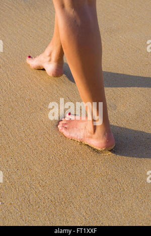Beach travel - woman walking on sand beach leaving footprints in the sand. Closeup detail of female feet and golden sand Stock Photo