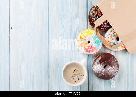 Colorful donuts in paper bag and coffee cup on wooden table. Top view with copy space Stock Photo
