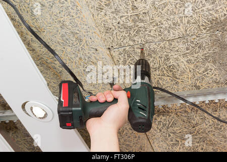 screwdriver drives screws into ceiling of fiberboard in a hand Stock Photo