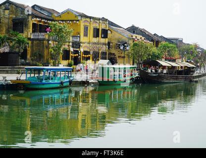Tourist boats moored on the riverside in Hoi An, Vietnam. Colonial style buildings line the streets. Stock Photo