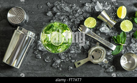 Glass of cocktail with lime, mint, ice. Drink making bar tools, shaker, ingredients Stock Photo