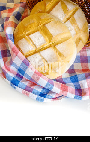 Two round loafs of bread wrapped in kitchen rag and weaved basket on white background. Copy space Stock Photo