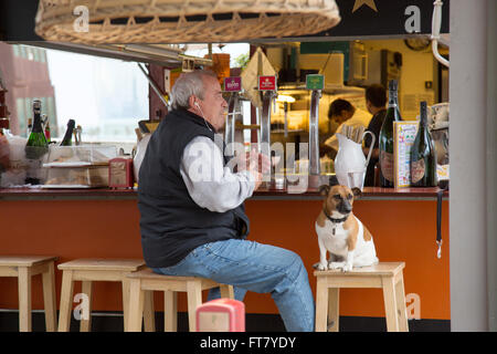 Man and dog sitting at bar on the beach in Barcelona, Spain. W Hotel in the distant background. Black and white version FWGAYR Stock Photo