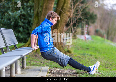 Young man is doing outdoor sports, fitness training, back dips, Stock Photo