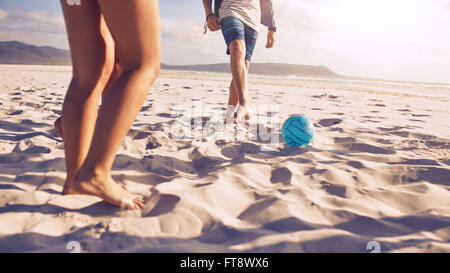 Low section portrait of young people playing soccer on the beach. Friends playing football on sandy beach, focus on ball and leg Stock Photo