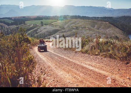 View of  a couple driving an ATV on dirt road in countryside. Young man and woman riding on a quad bike on country road. Stock Photo