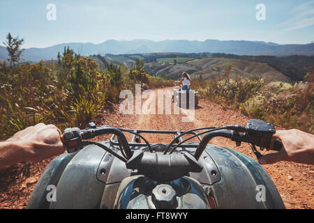 View from a quad bike in nature. Woman in front driving off road on an all terrain vehicle. POV image of a quad biker following Stock Photo
