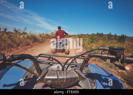 View from a quad bike in nature. Man in front driving off road on an all terrain vehicle. POV shot. Stock Photo