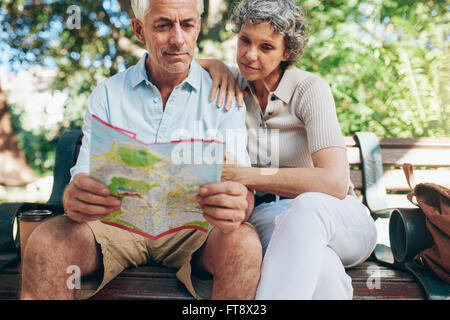 Senior tourist sitting on a park bench reading city map. Man and woman using city guide for finding their location. Stock Photo