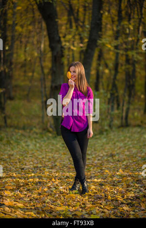 Girl holding yellow leaf. Beatiful teenager girl wearing a purple shirt and holds a yellow leaf in a autumn woods. She is standi Stock Photo
