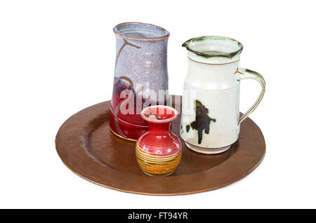 trio of small ceramic pottery includes vase pitcher and ewer on copper serving tray isolated against white Stock Photo