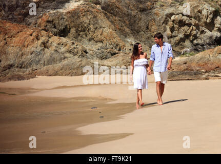 Cheerful couple walking on beach on rock background Stock Photo