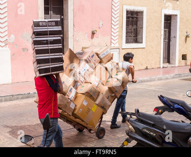Shop Deliveries. Two men, one with a pull cart and one with shoe boxes piled high walk the cobbled street to deliver merchandise Stock Photo