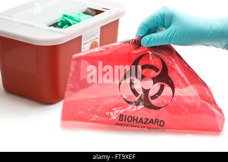 Health care worker's gloved hand with hazardous waste container and bag. Stock Photo