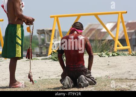 Catholic penitents whip themselves in self flagellation during the re-enactment of the crucification of Christ during Good Friday observances in San Fernando, Pampanga, Philippines. The festival known as Kapampangan includes self flagellation, carrying wooden crosses, crawling on rough pavement, and slashing and whipping to draw blood. Stock Photo