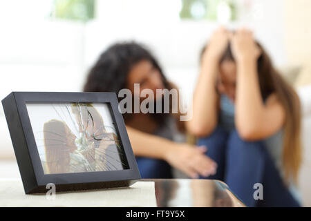 Sad wife after a breakup with a friend comforting her in the living room Stock Photo