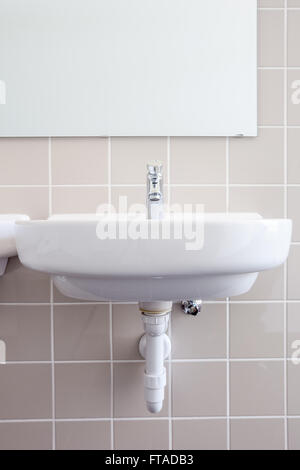 in an public restroom hangs on an wall of an white sink Stock Photo